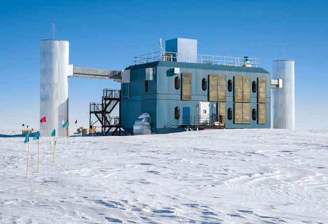 The IceCube research station, a rectangular building with three pillars attached, sitting on snowy ground.