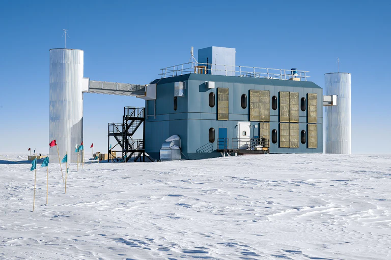 The IceCube research station, a rectangular building with three pillars attached, sitting on snowy ground.