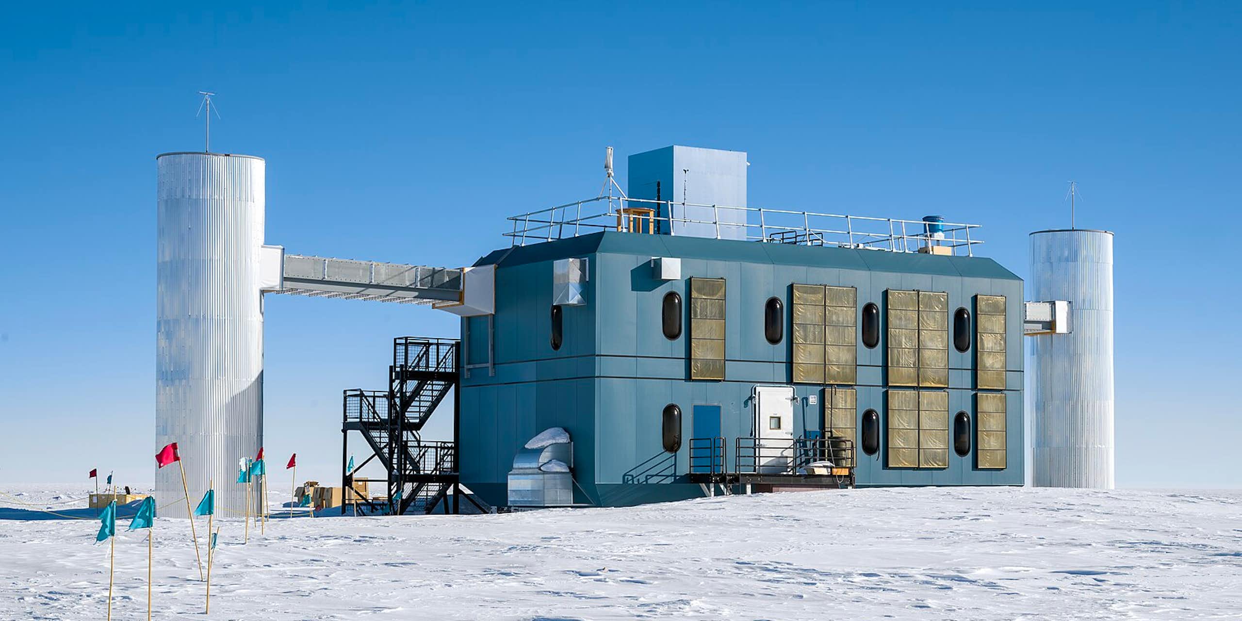 The IceCube research station, a rectangular building with three pillars attached, sitting on snowy ground.