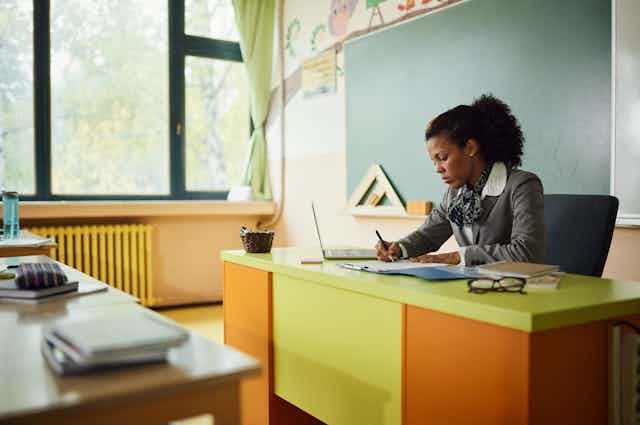 A teacher sits at her desk grading papers.