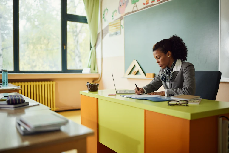 A teacher sits at her desk grading papers.