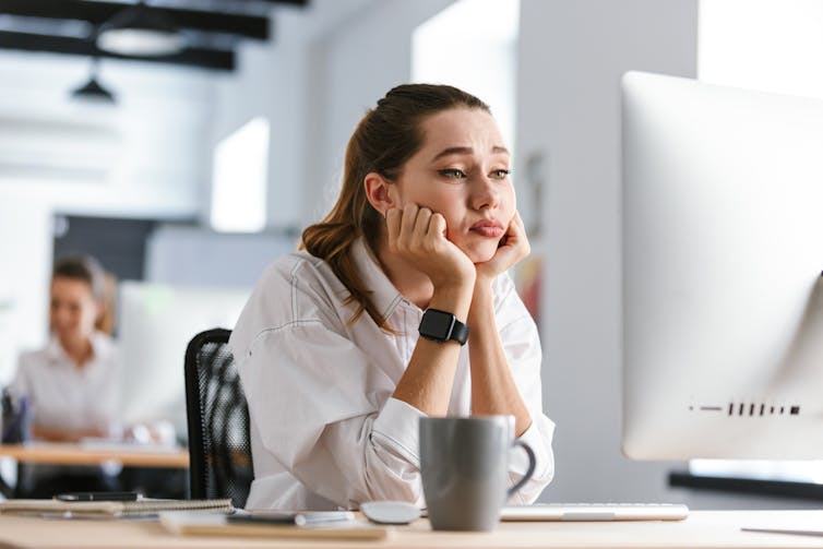 A young woman sitting at a desk with her chin in her hands, looking very bored