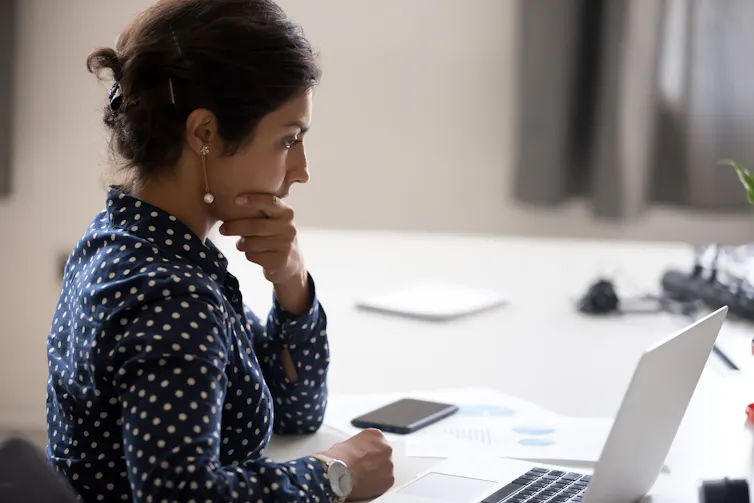 A young South Asian women looks at an open laptop with a serious, concentrated look on her face