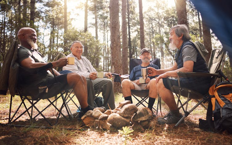 A group of men are sitting outside in a wooded area.