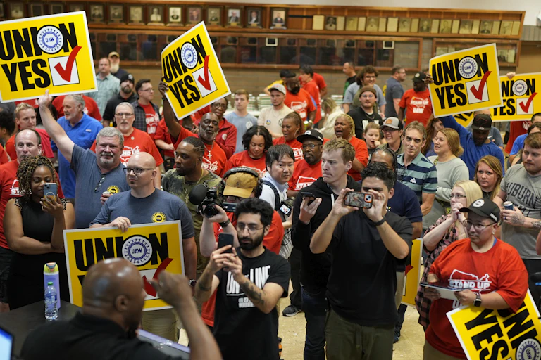 People in t-shirts hold yellow signs that say Union Yes with a checkmark aloft.