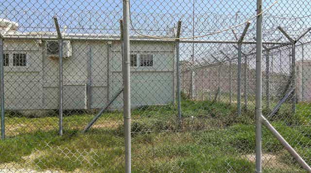 A hut is seen behind a wire fence.