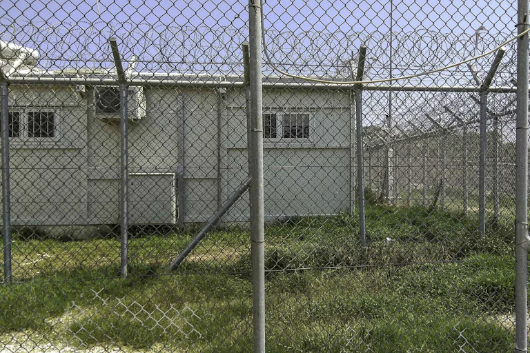 A hut is seen behind a wire fence.