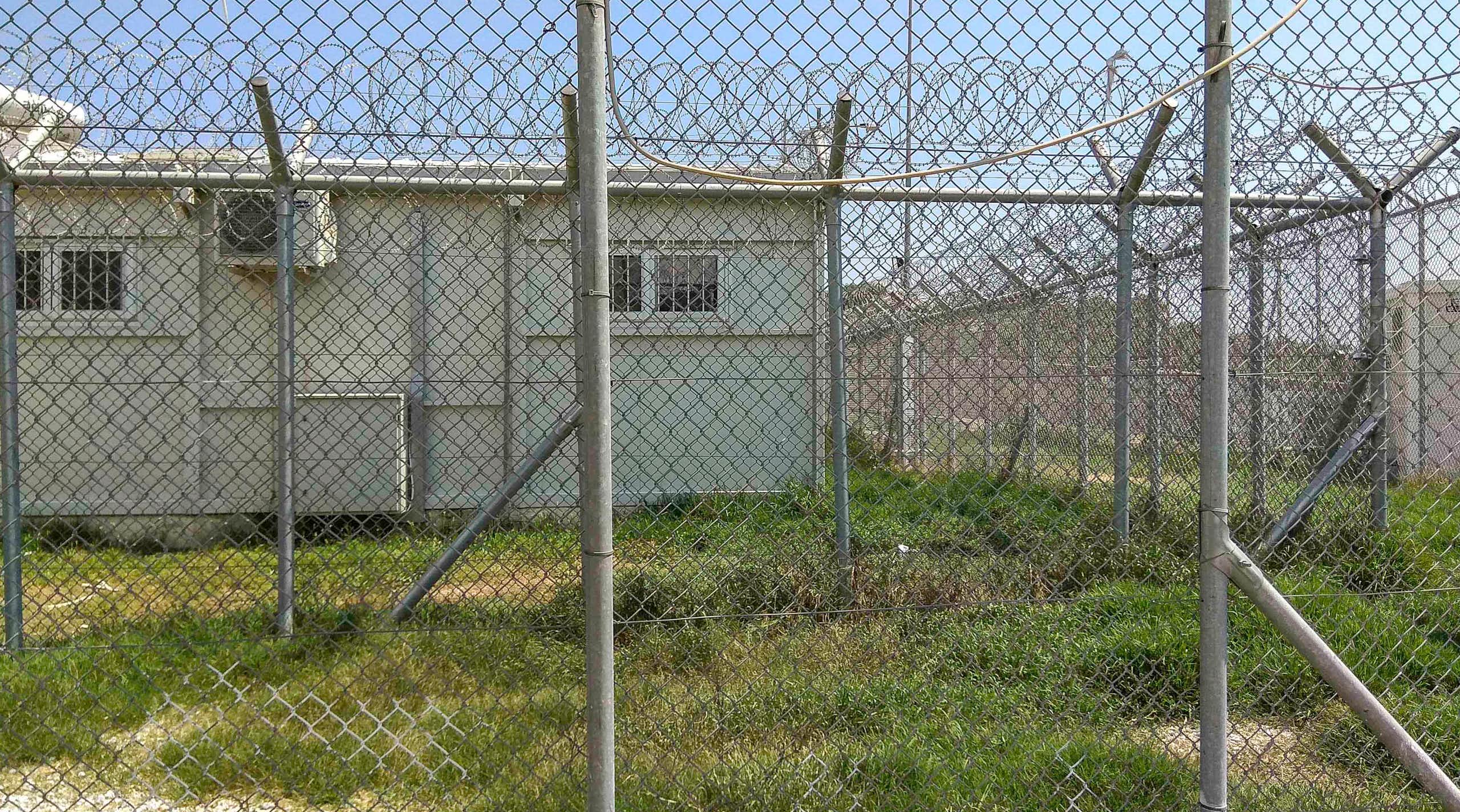 A hut is seen behind a wire fence.
