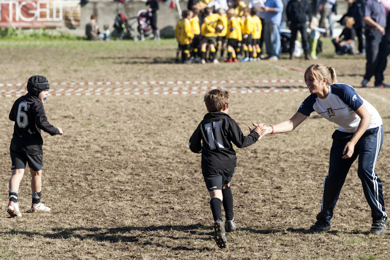 A female coach high-fives a junior rugby player
