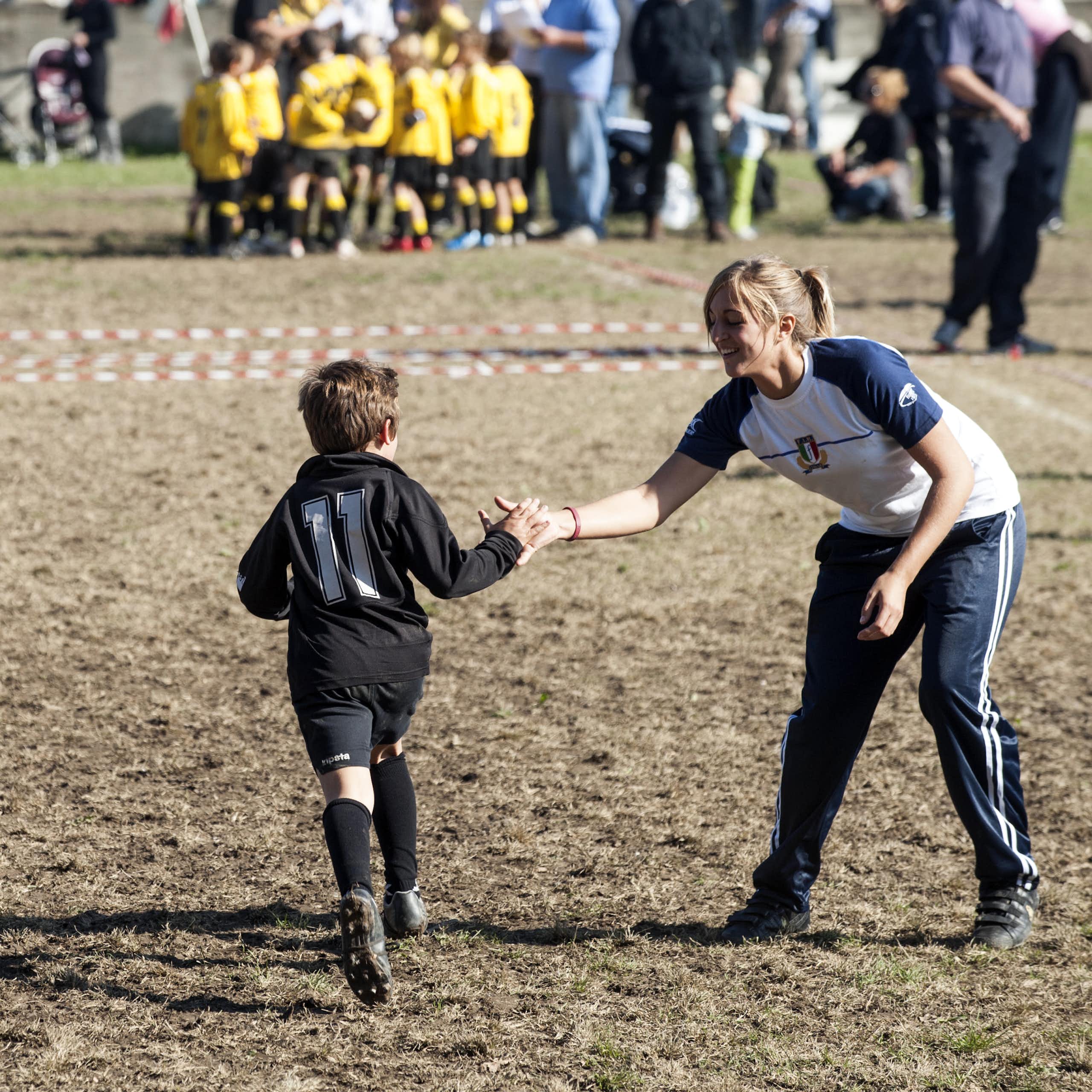 A female coach high-fives a junior rugby player