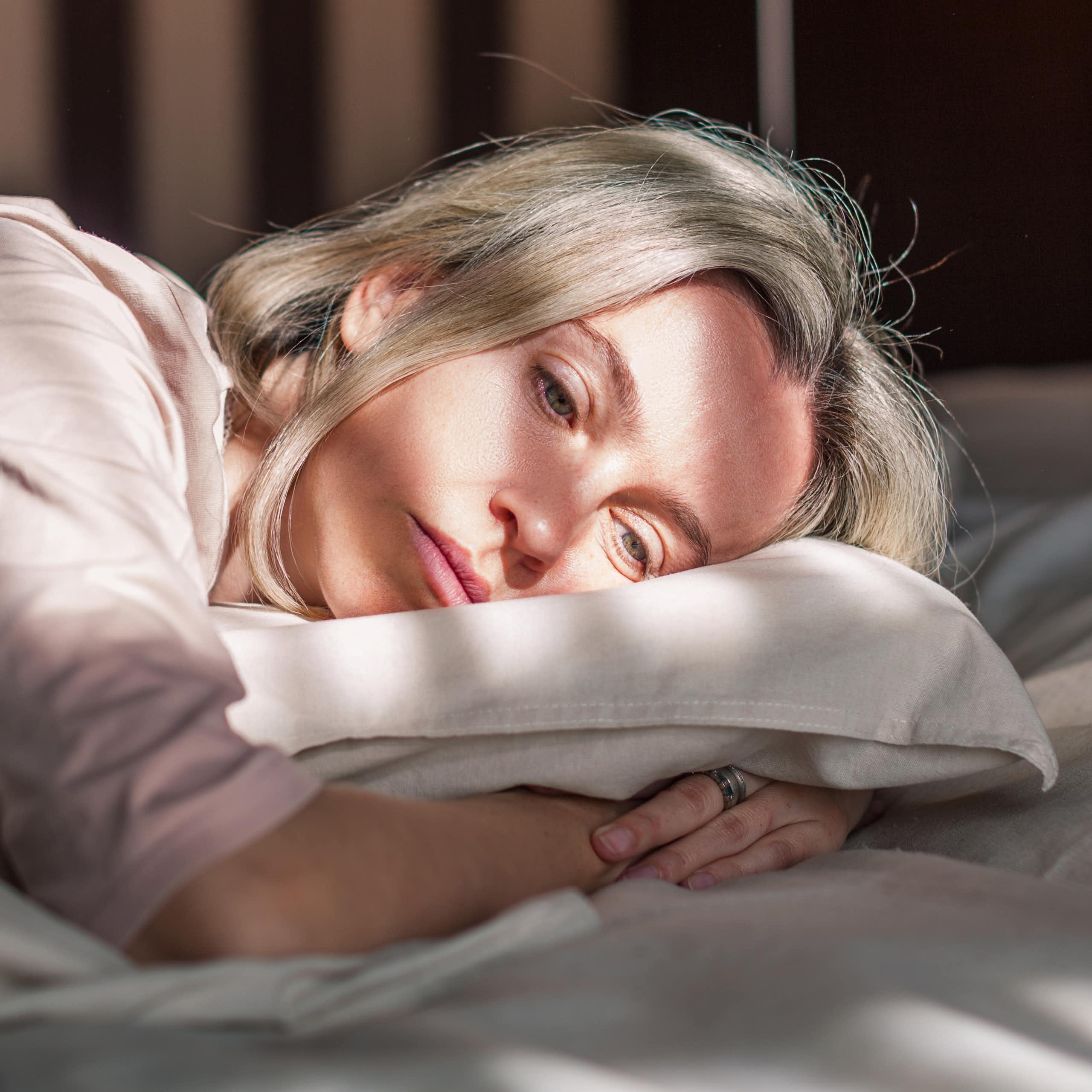 Woman lays in bed, looking sad