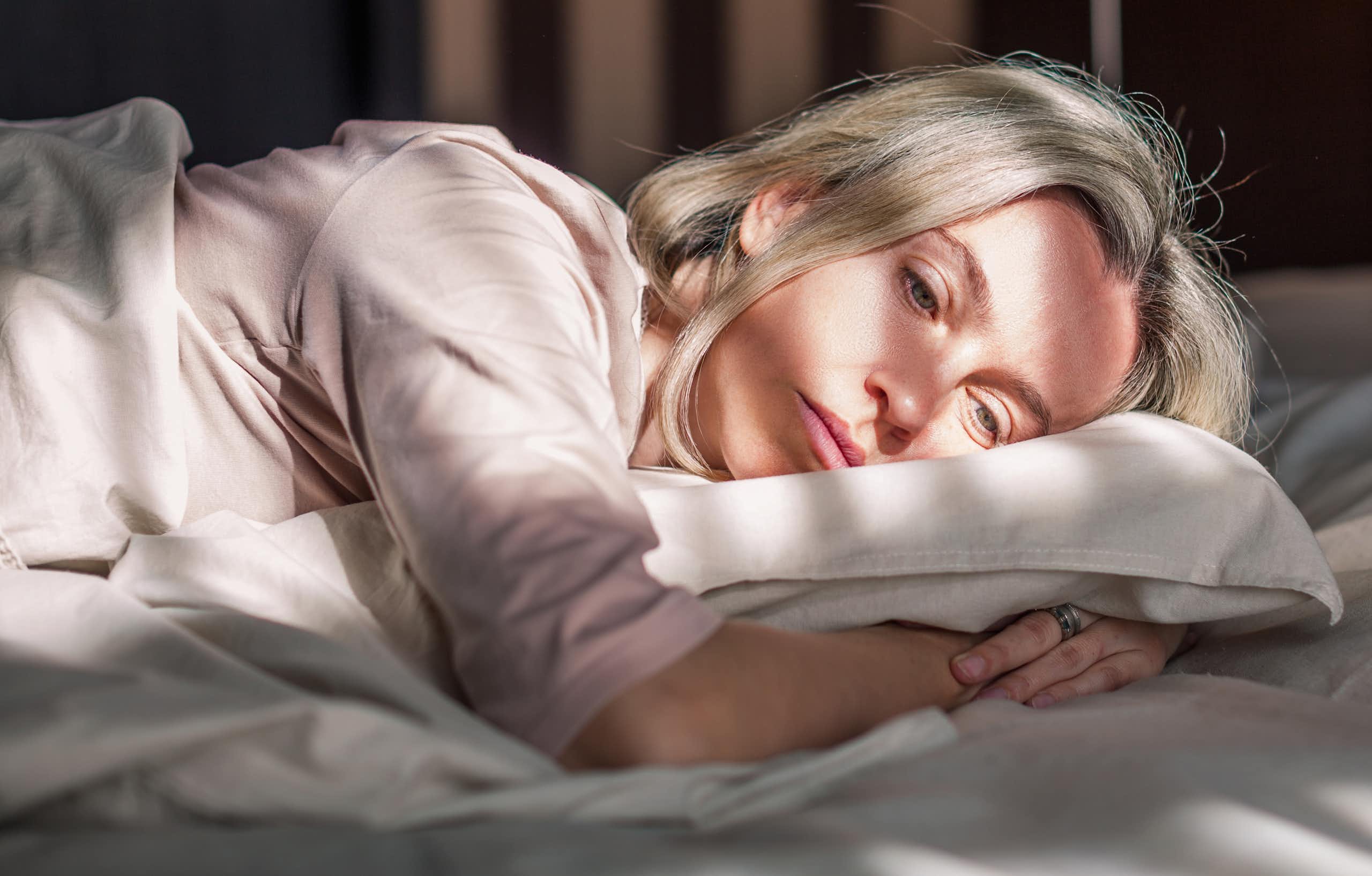 Woman lays in bed, looking sad