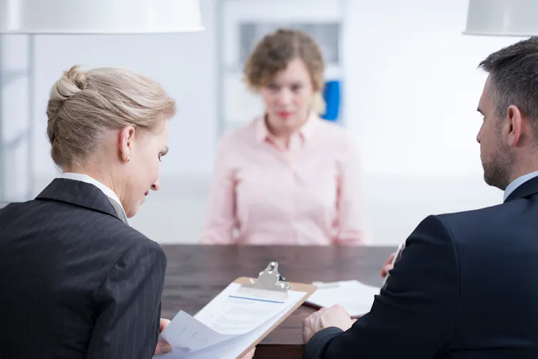 Man and woman check some paperwork while a woman sits nervously on the other side of the desk