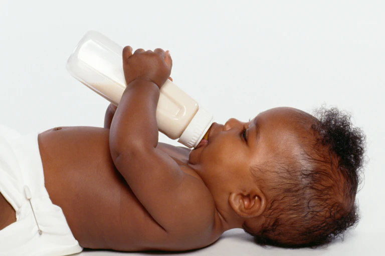 A baby lying on its back and drinking out of a bottle