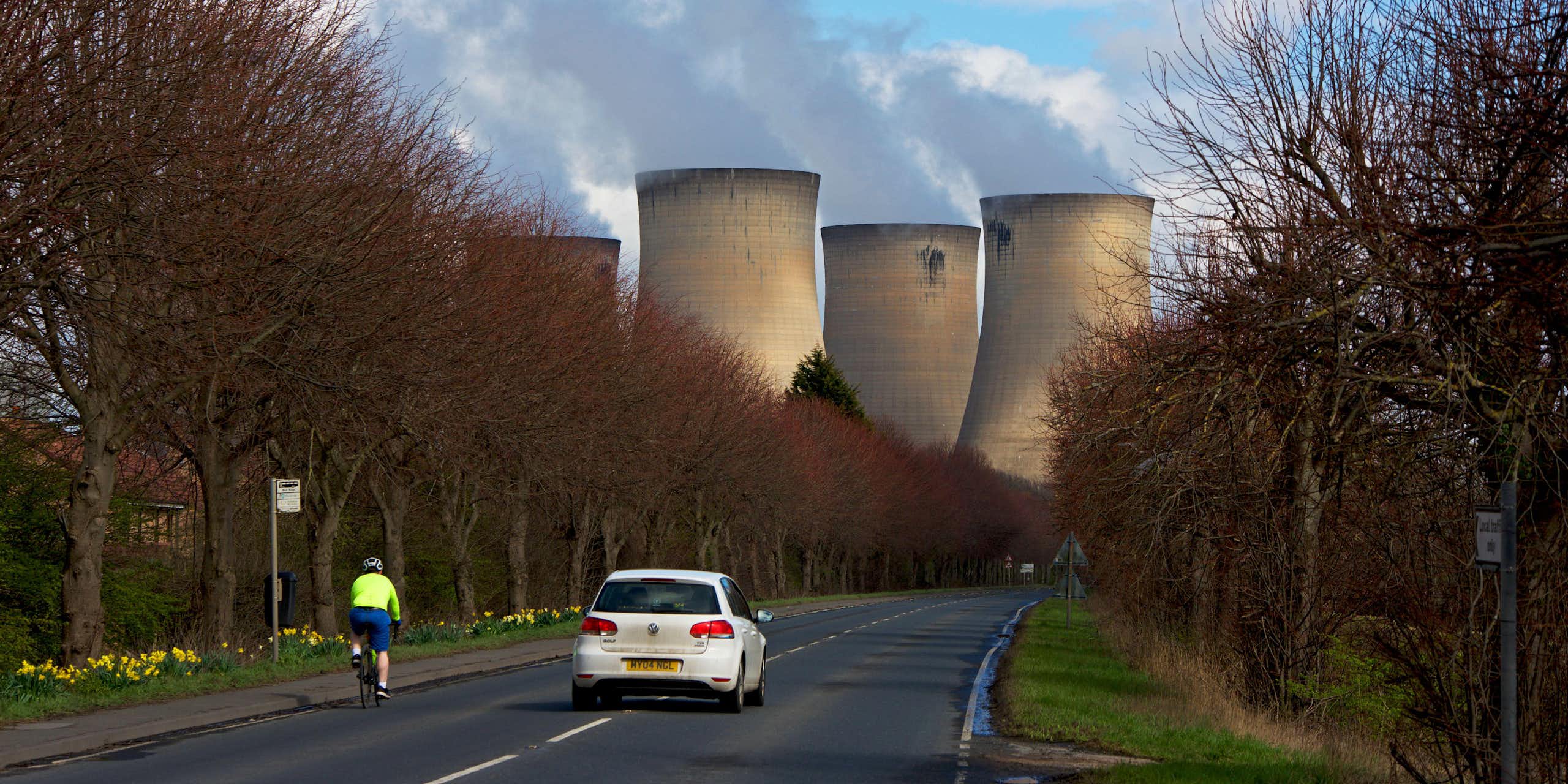 A cyclist and car on a road leading to a power station.