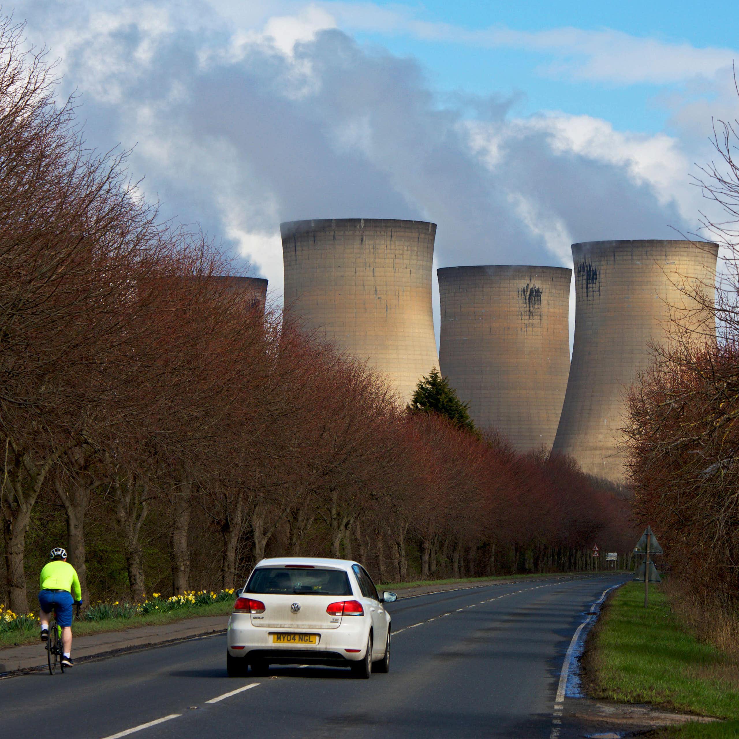 A cyclist and car on a road leading to a power station.