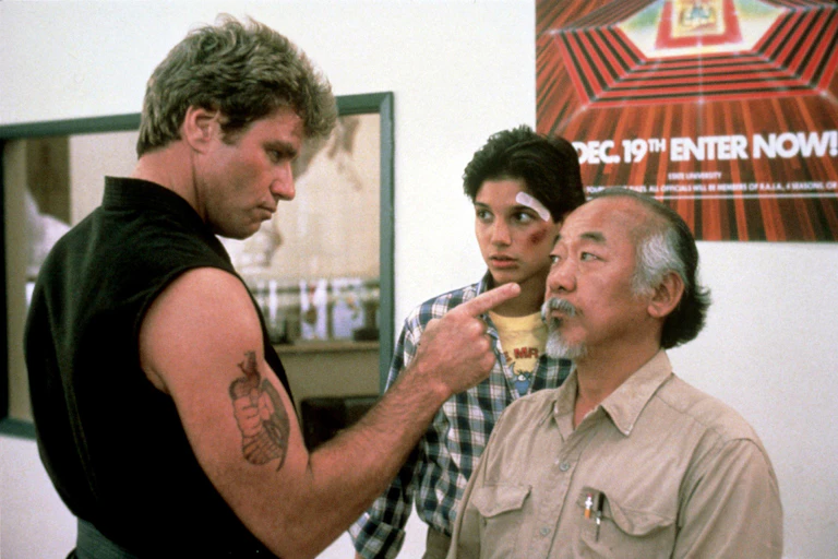 A large man in a sleeveless black top points his finger at a shorter man and a teenager.