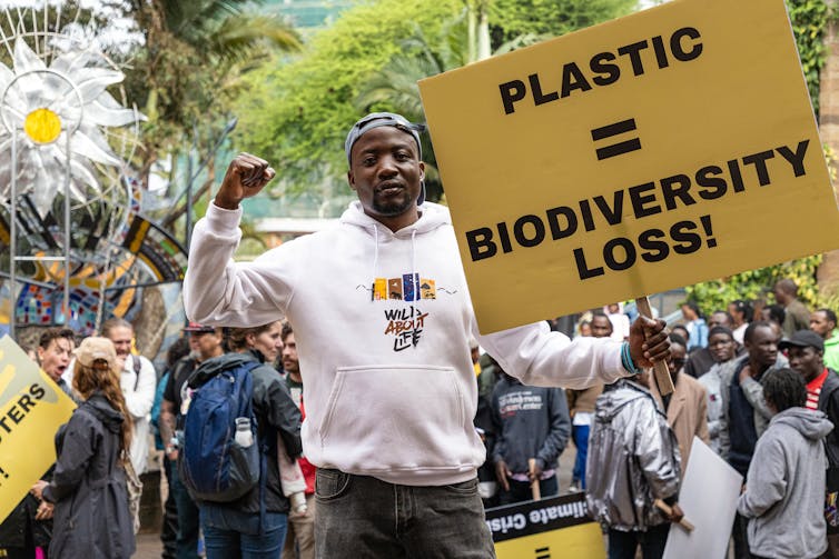 Man holds sign saying 'plastic = biodiversity loss'