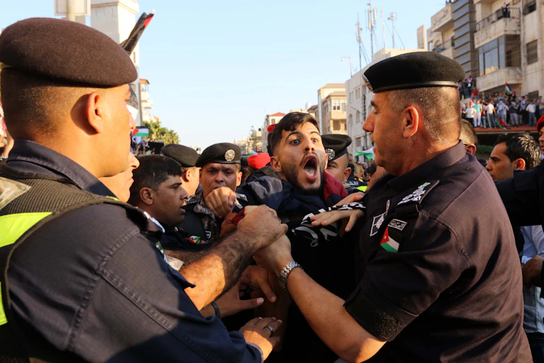 A protestor with his mouth wide open being held back by security personnel.