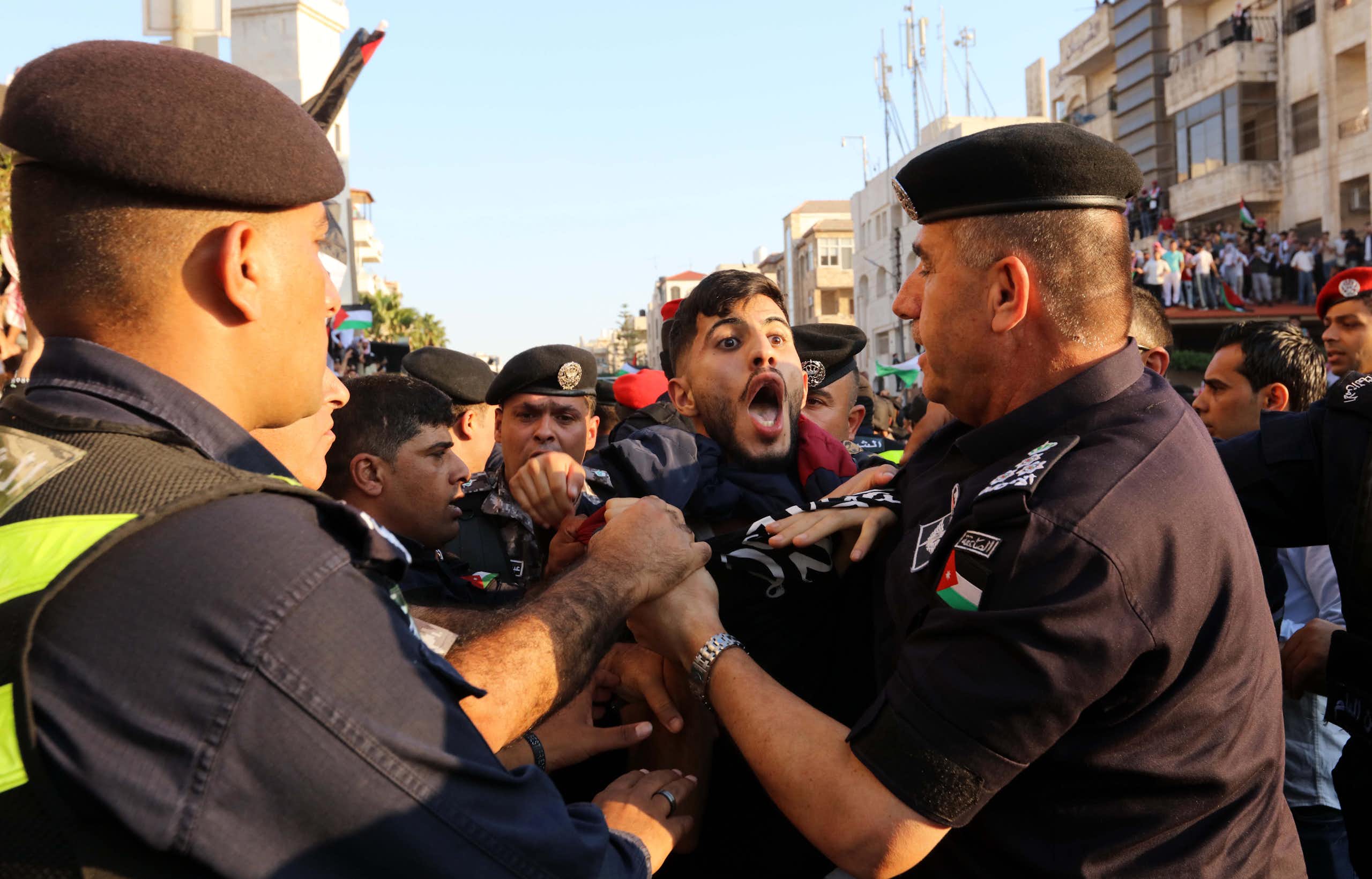 A protestor with his mouth wide open being held back by security personnel. 