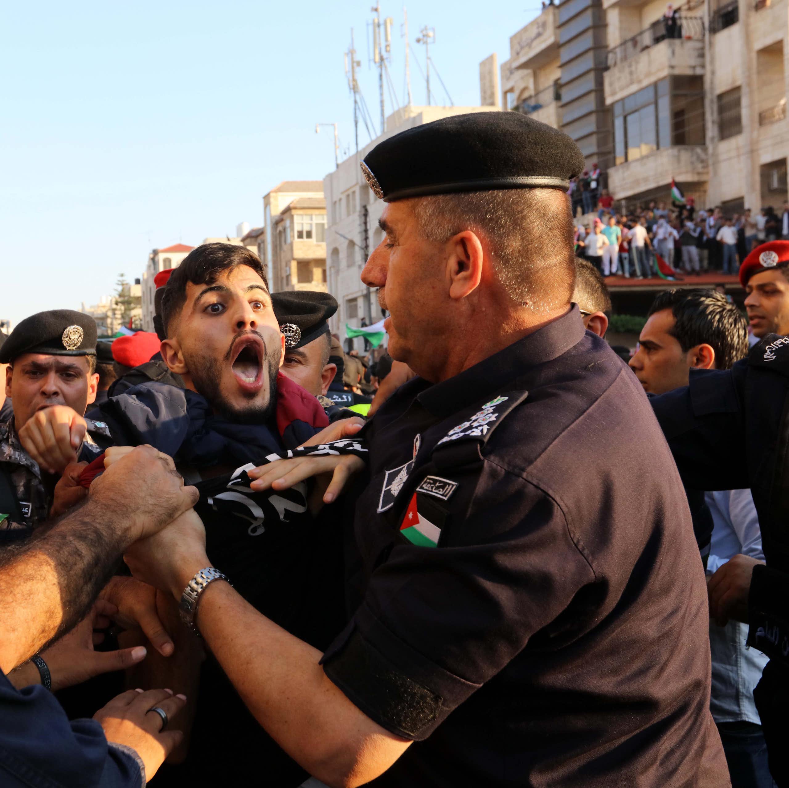 A protestor with his mouth wide open being held back by security personnel. 