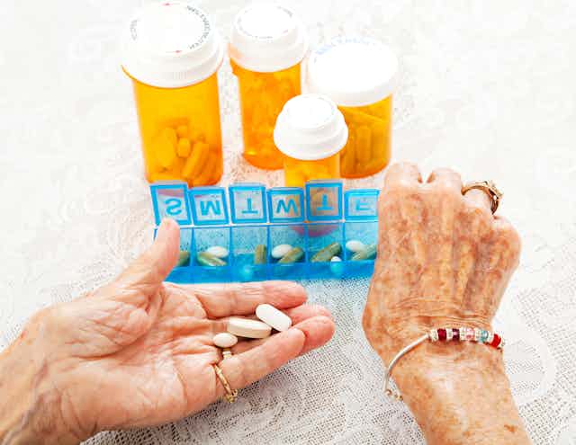 Les mains d'une personne âgée en train de prendre des médicaments dans un boîtier