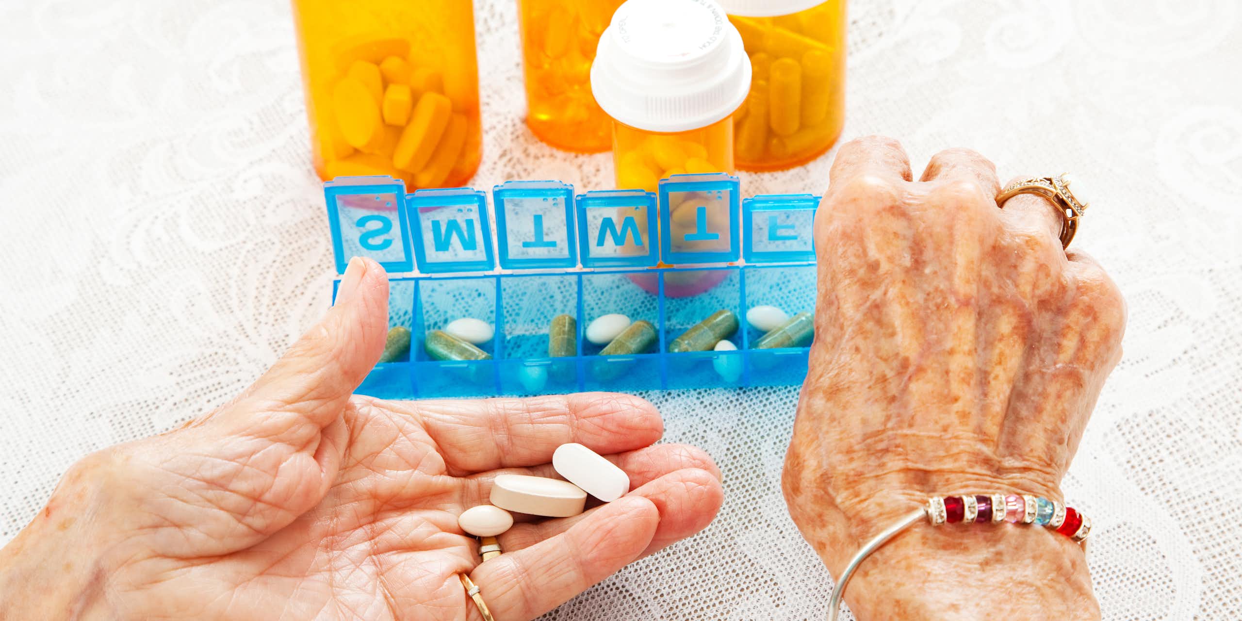 Les mains d'une personne âgée en train de prendre des médicaments dans un boîtier