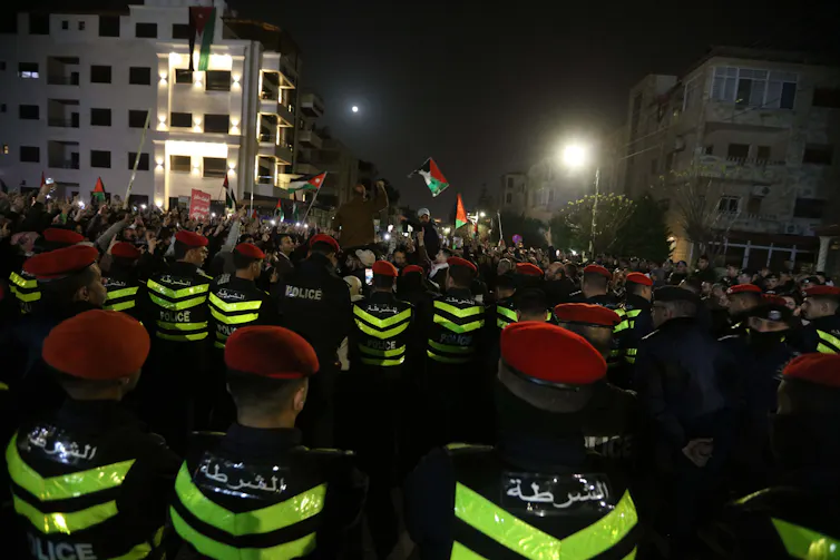 Policemen watching a crowd of protestors waving Jordanian flags.