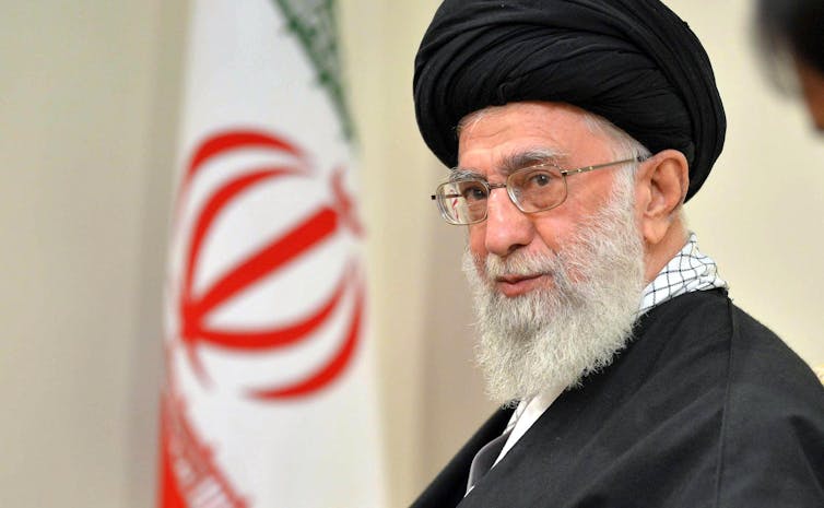 A close-up shot of Ali Khamenei in front of an Iranian flag.