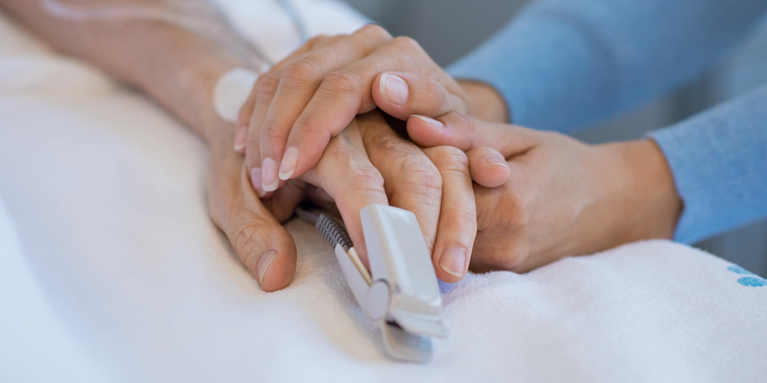 Photo d’une personne tenant la main d’une autre, alitée dans un hôpital.