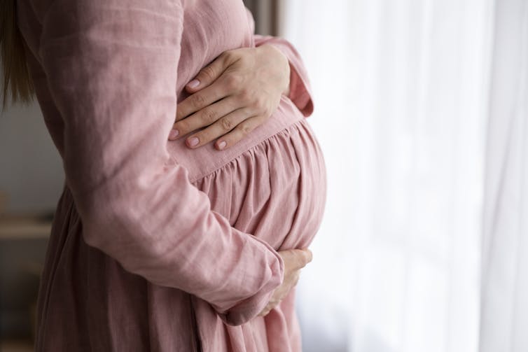 Pregnant woman holds belly in profile.