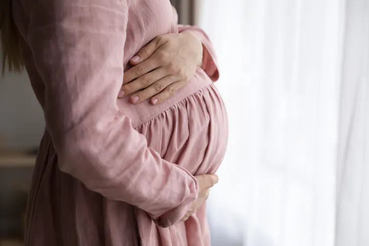 Pregnant woman holds belly in profile.