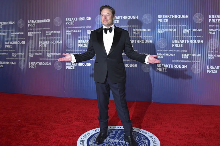 Elon Musk standing on a red carpet.