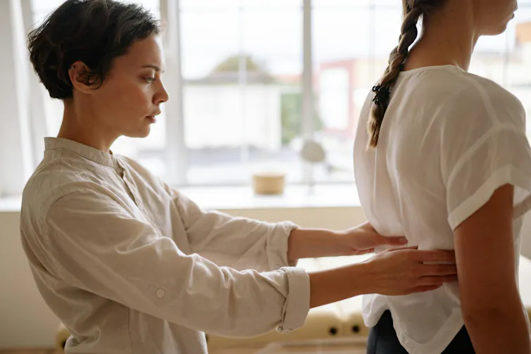 A medical practitioner examines a patient's lower back.