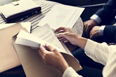 Unidentified man goes through a folder while another man sits nearby