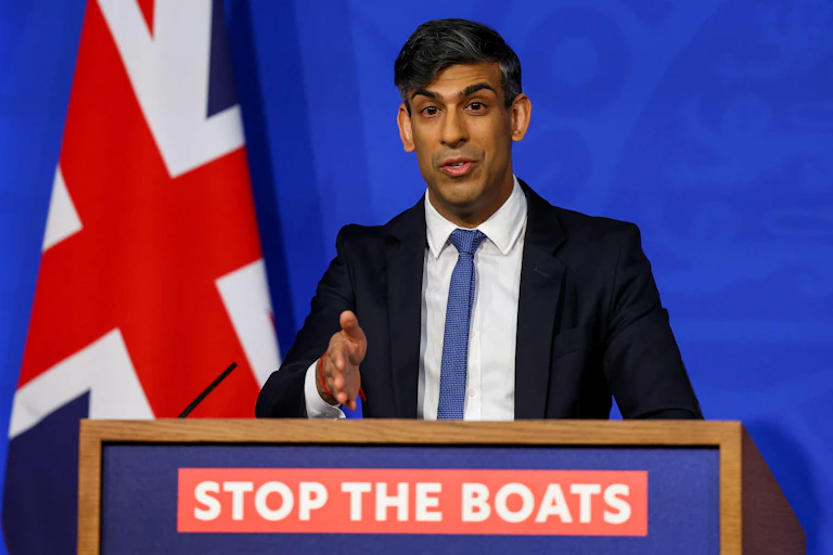 Rishi Sunak speaking and gesturing decisively at a podium that reads Stop the Boats