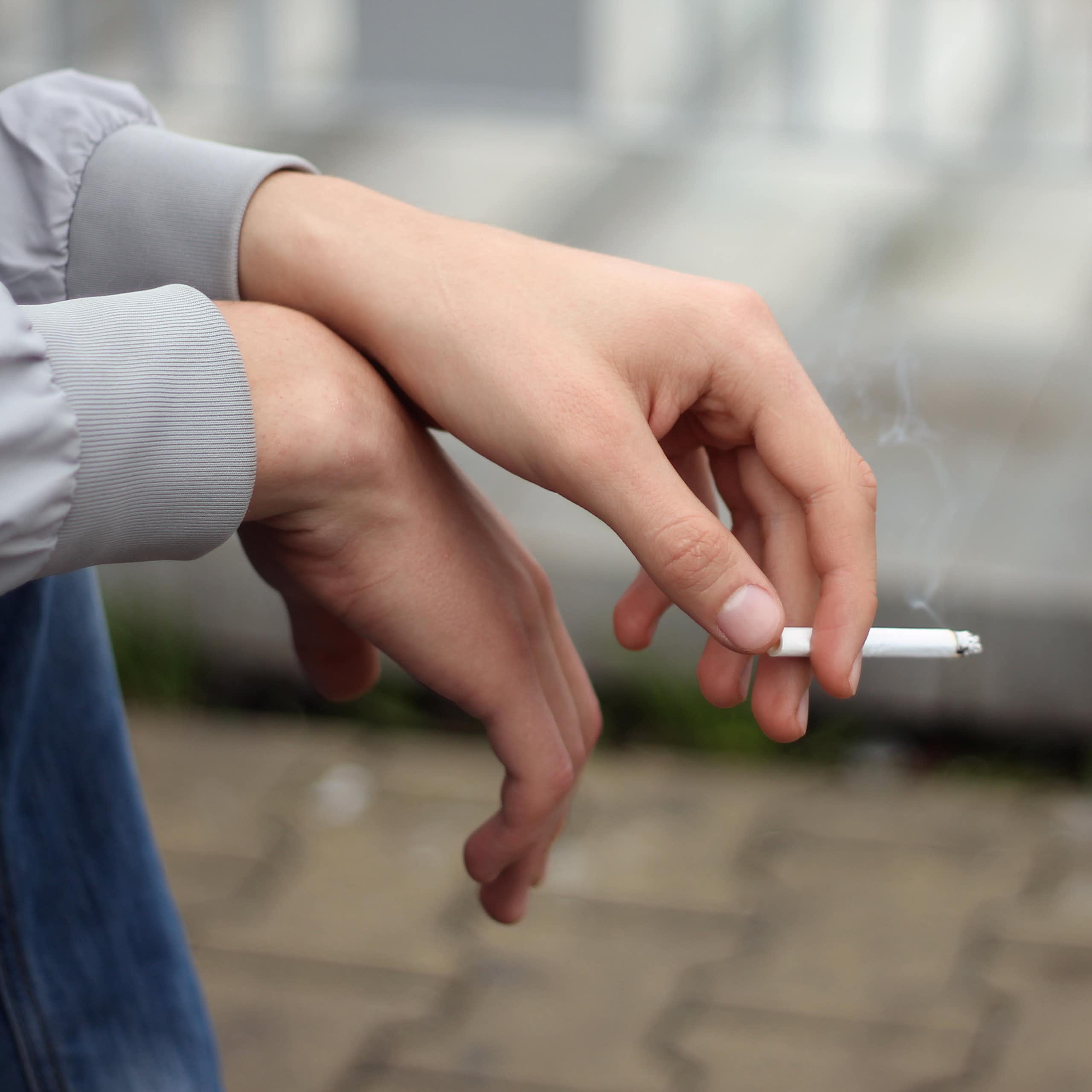 A person holds a lit cigarette in their hand.