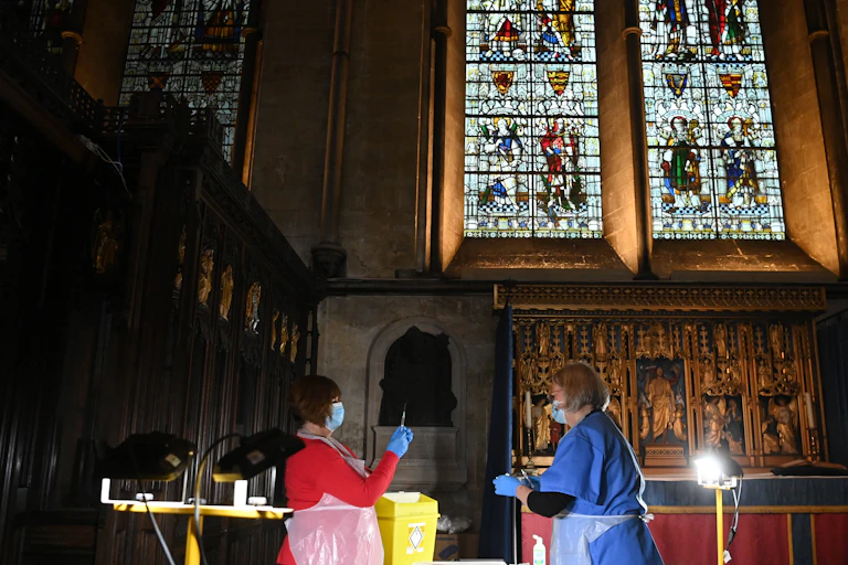 Two women in PPE prepare vaccines inside a church.