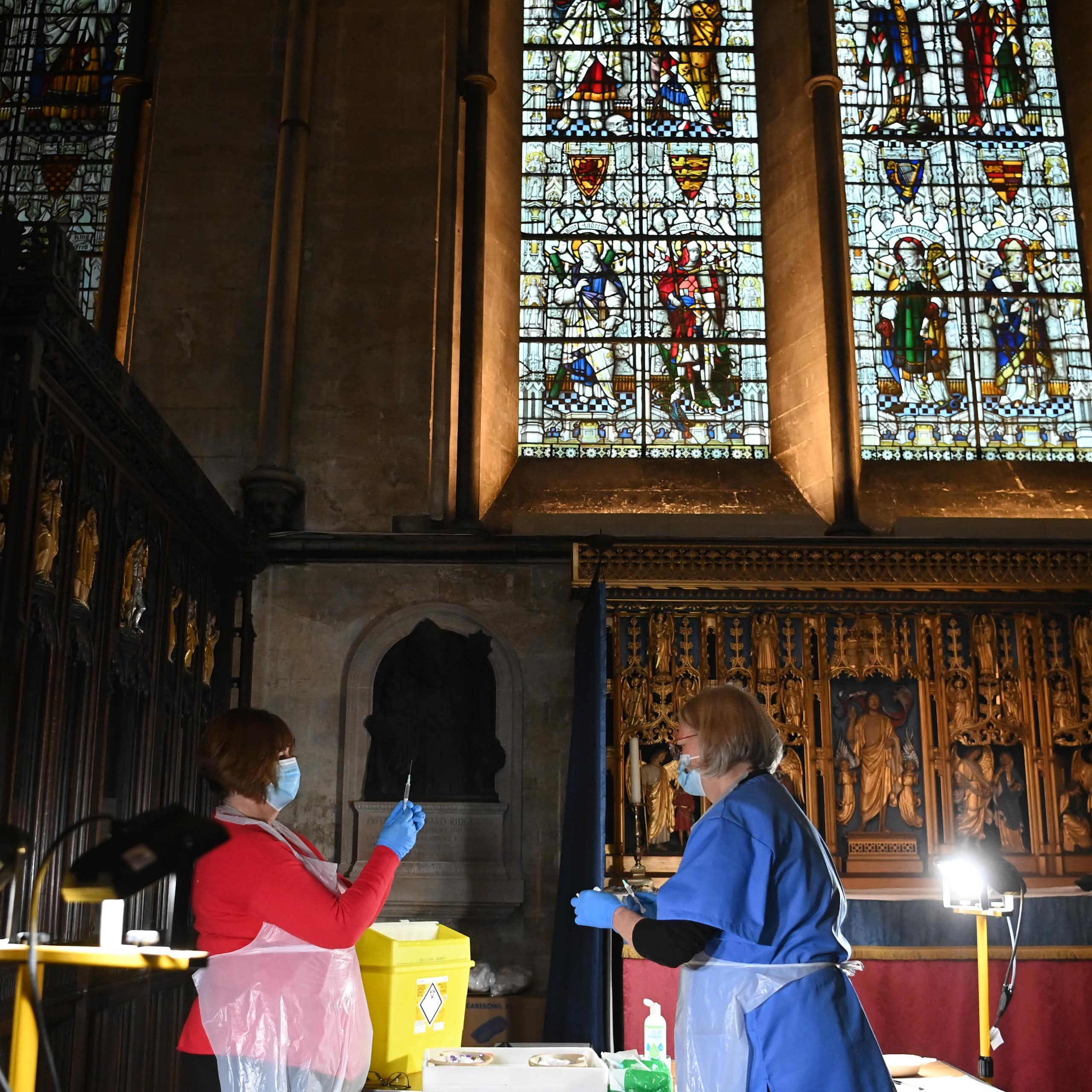 Two women in PPE prepare vaccines inside a church. 