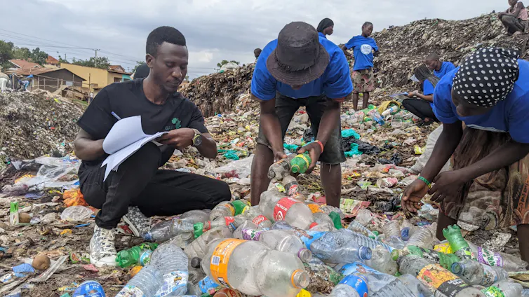 Three men kneeling over a pile of single-use plastic beverage bottles. One man has a clipboard and is counting the number of bottles.