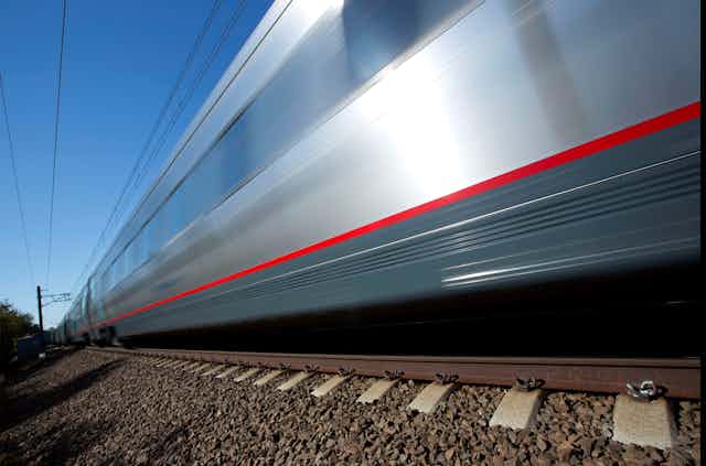 A silver train speeds through the frame, slightly blurred