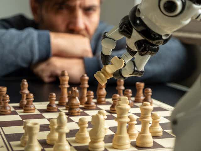 Um braço robótico agarra uma peça de xadrez em um jogo contra um humano