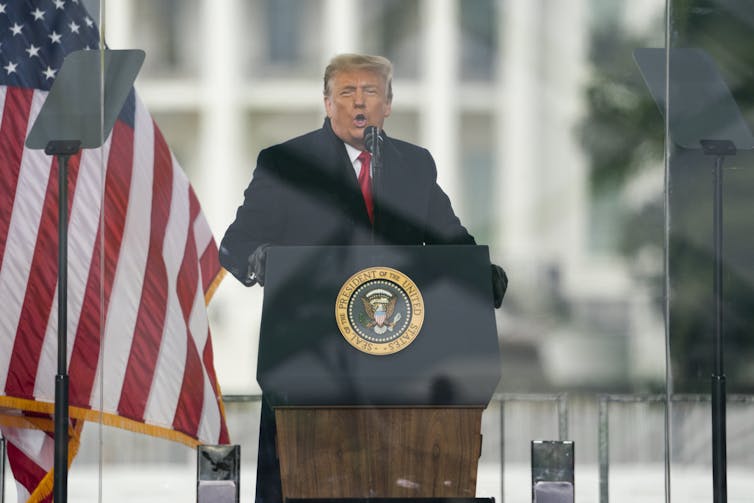 A man stands at a lectern in front of an American flag.