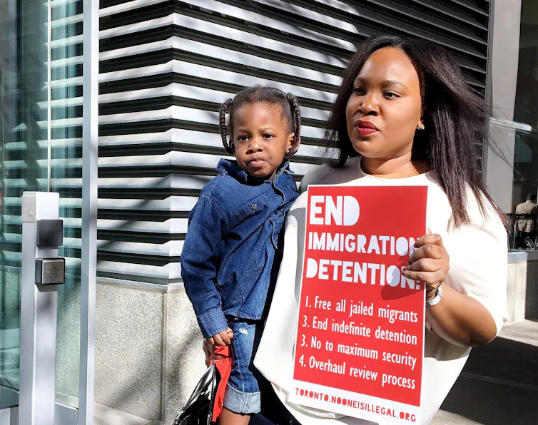 A woman carrying a young child with a placard: End immigration detention