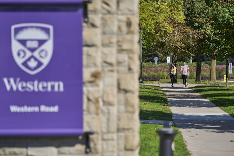 A purple Western University sign with people walking along a path in the background.