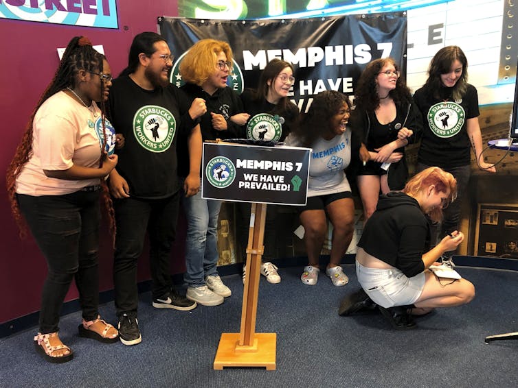 Young people in Starbucks-themed t-shirts lock arms and smile.