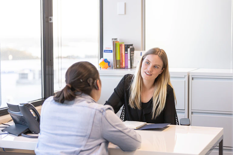 two women sit across a desk, one is wearing hearing apparatus