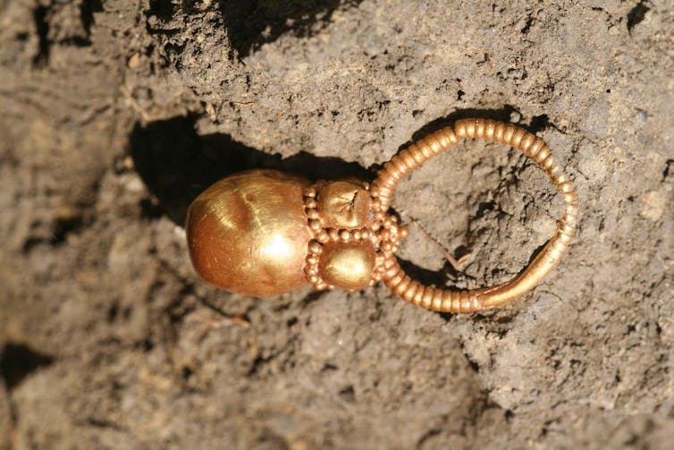 Photo of a small gold earring against a background of dirt.