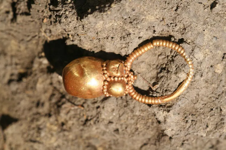 Photo of a small gold earring against a background of dirt.