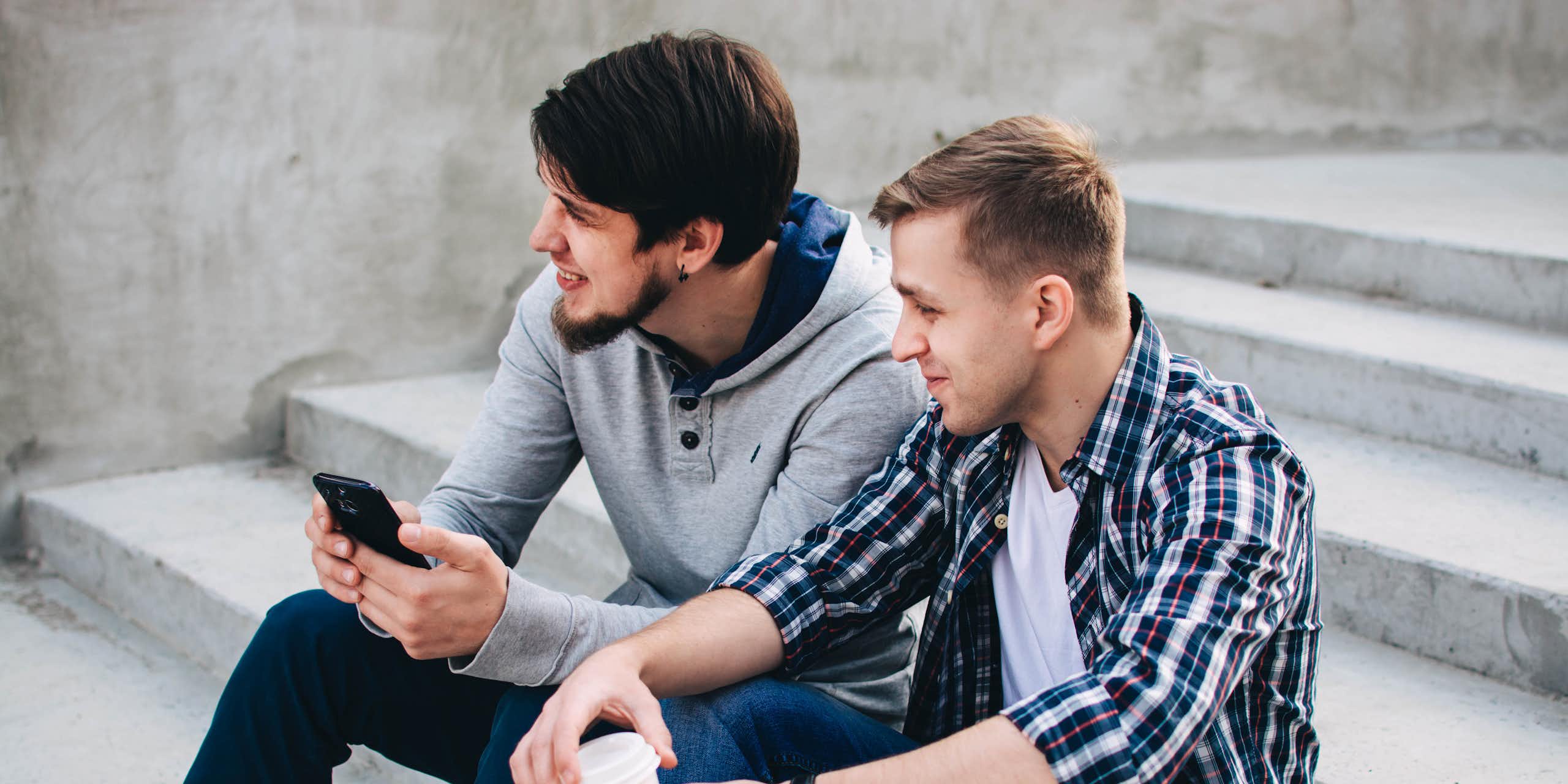 Two young men sit and chat on concrete steps